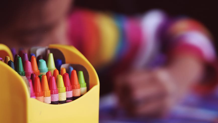 Ceras de colores con un niño detrás